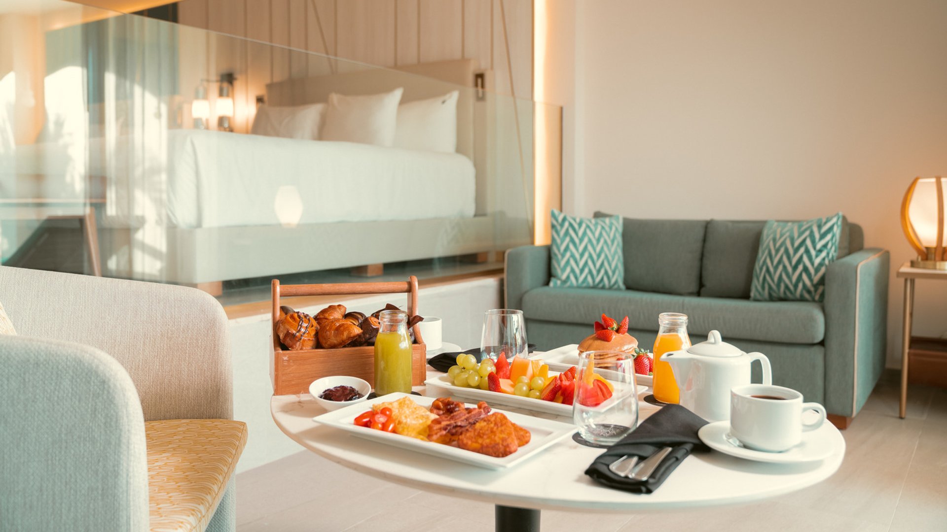 Luxurious hotel suite with breakfast table, sofa, bed, and glass partition at Hard Rock Punta Cana.